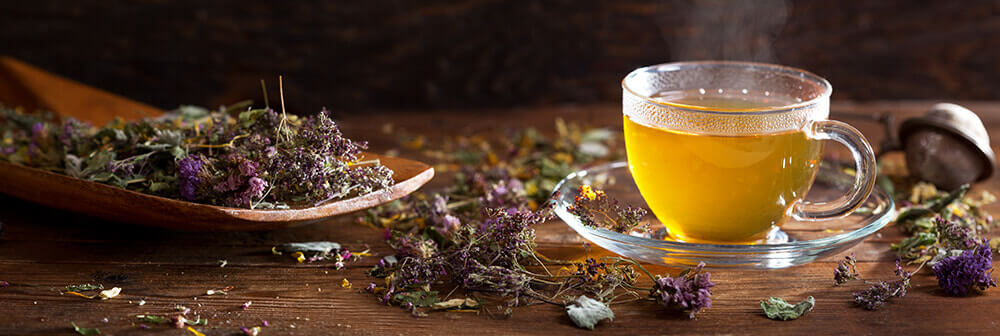 Tasse de tisane dorée et plantes séchées posées sur un plateau